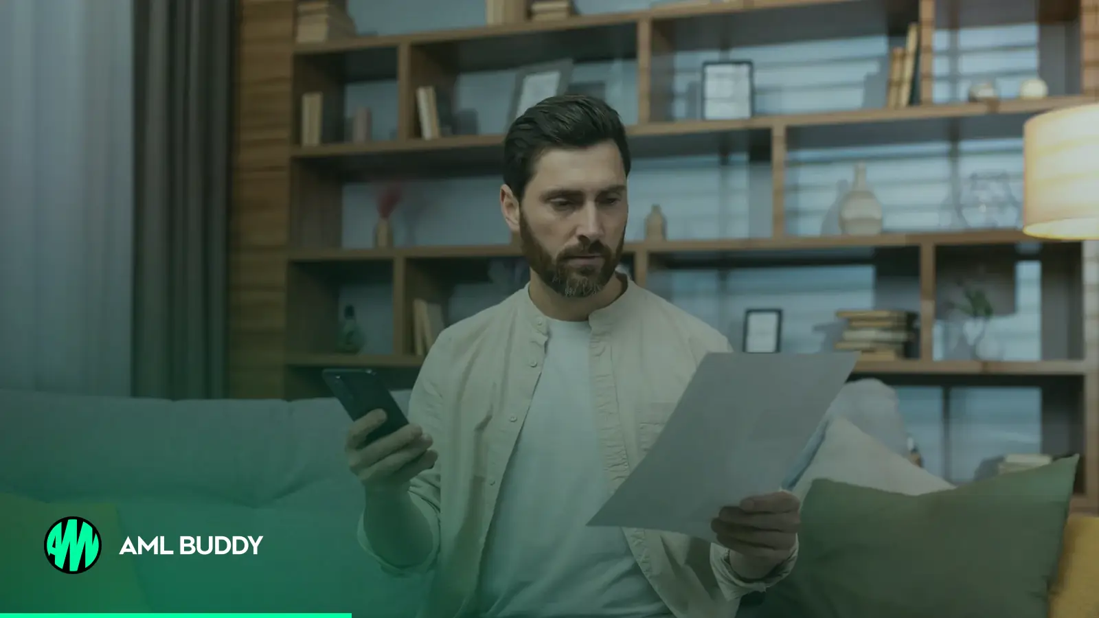 A man at home checking a letter against his phone before paying